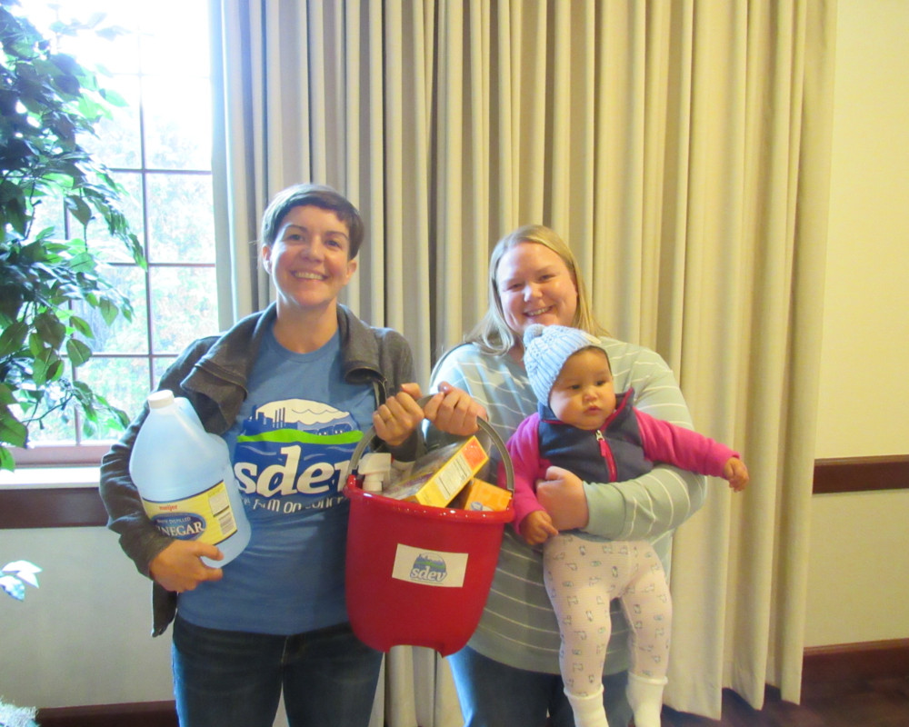 Two people holding a baby and a bucket of toxic-free supplies at SDEV event in Dearborn Michigan 