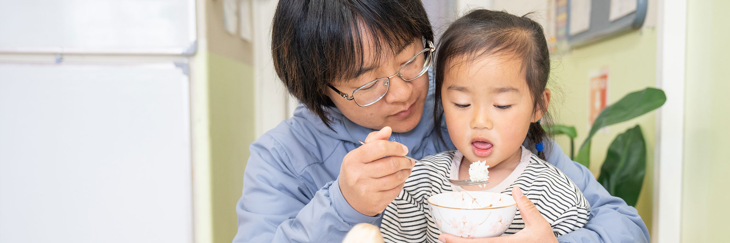 Woman helping a small child spoon rice from a bowl