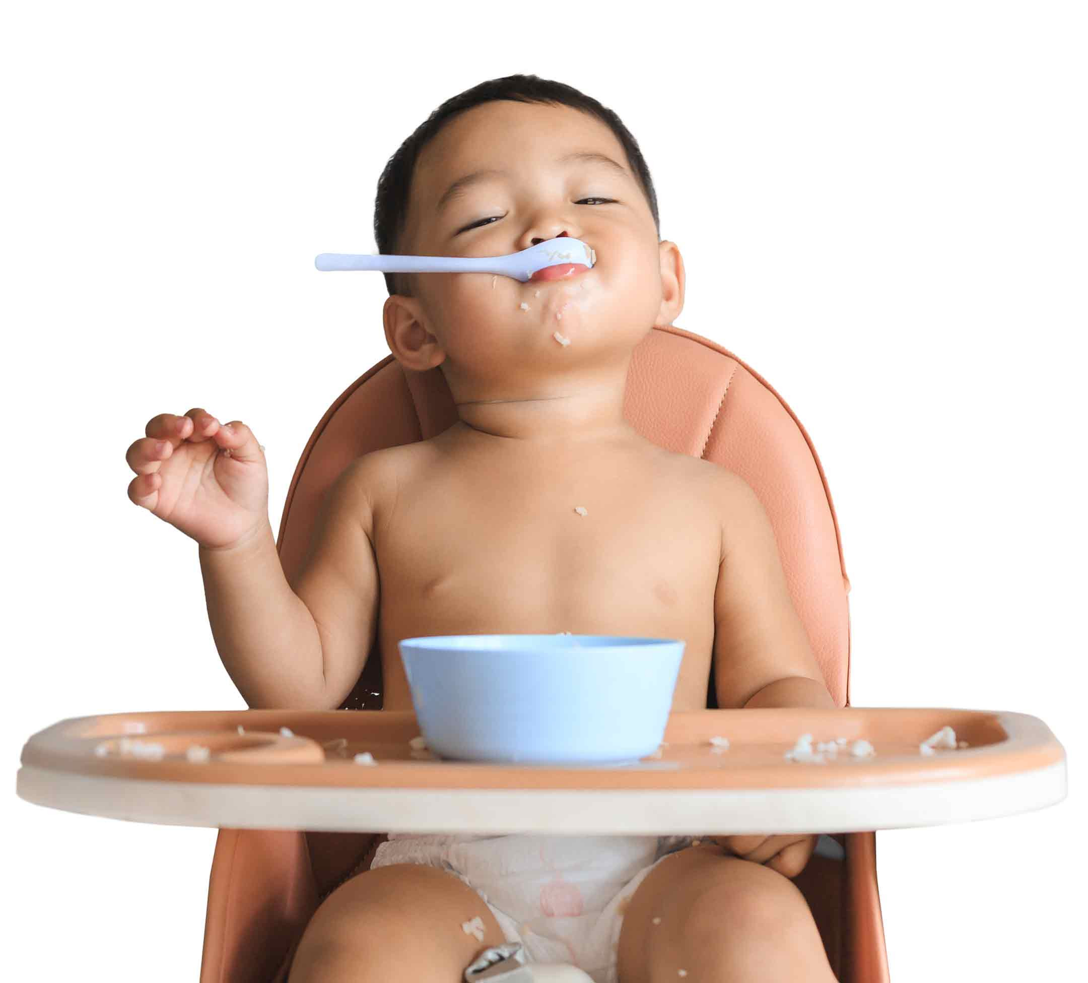 Baby in highchair with spoon of rice in his mouth